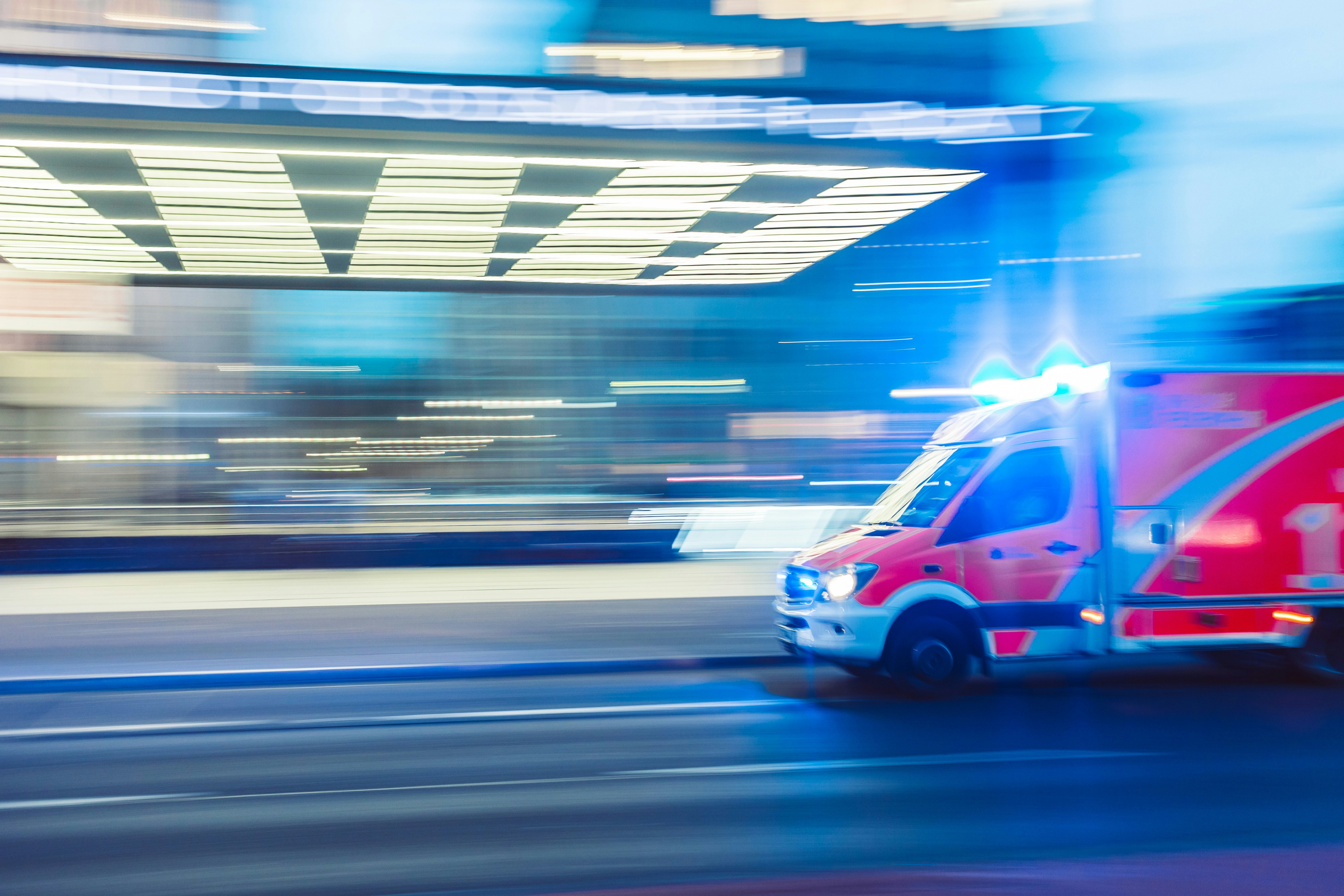 Motion-blurred ambulance with flashing lights speeding through a city street at night