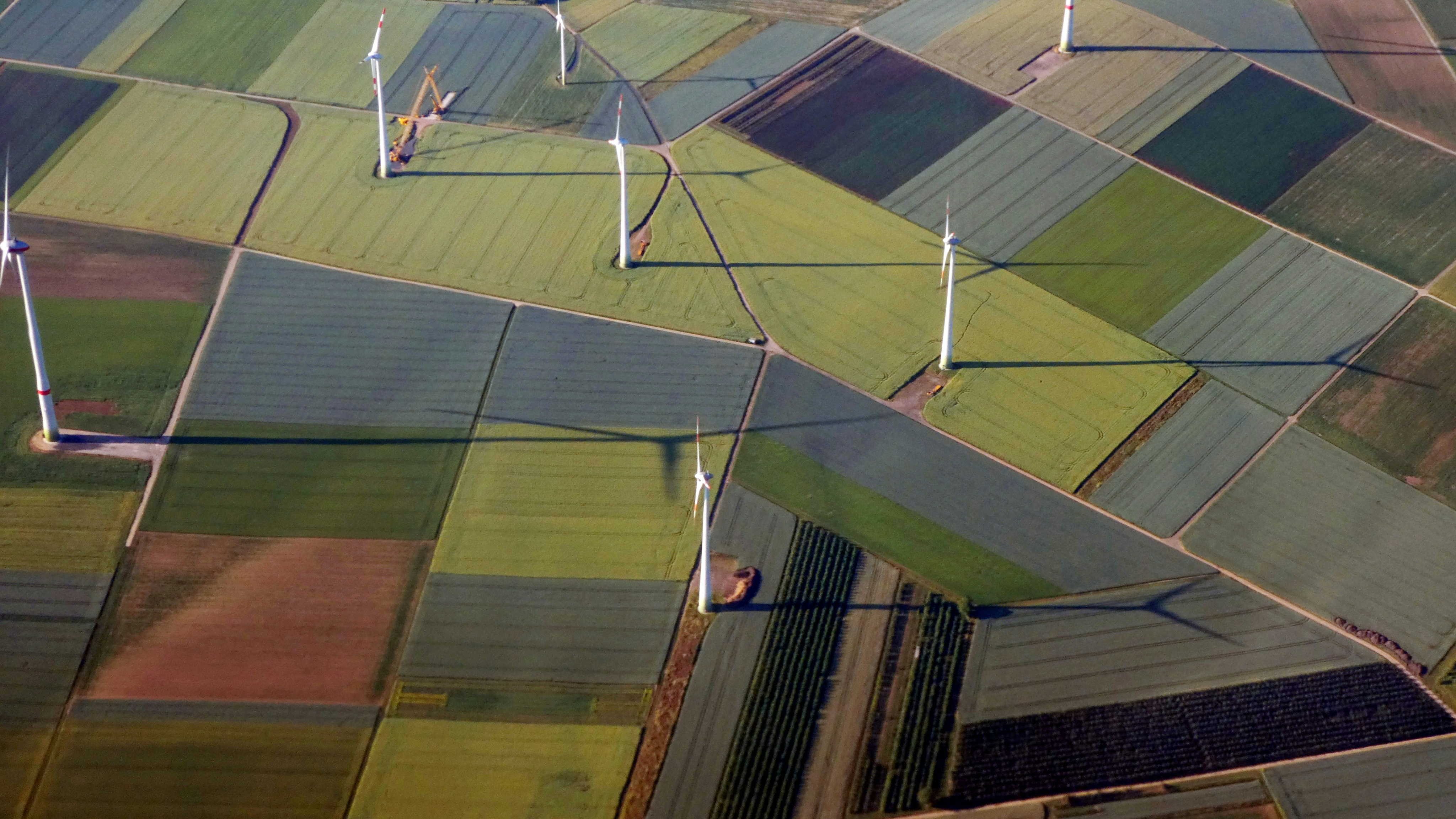 Aerial view of wind turbines scattered across colorful farmland fields
