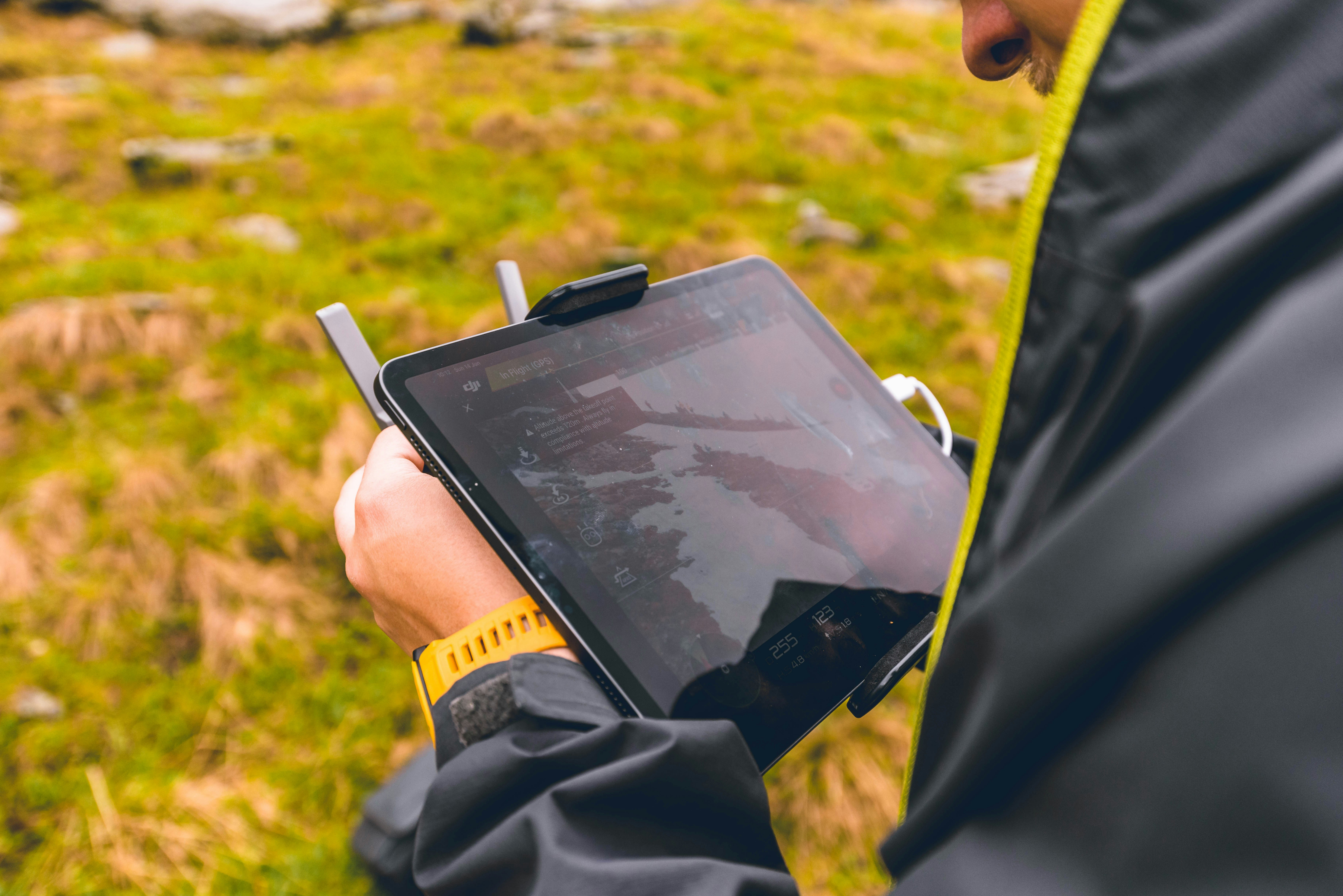 Person in a rain jacket holding a tablet drone controller over grassy terrain