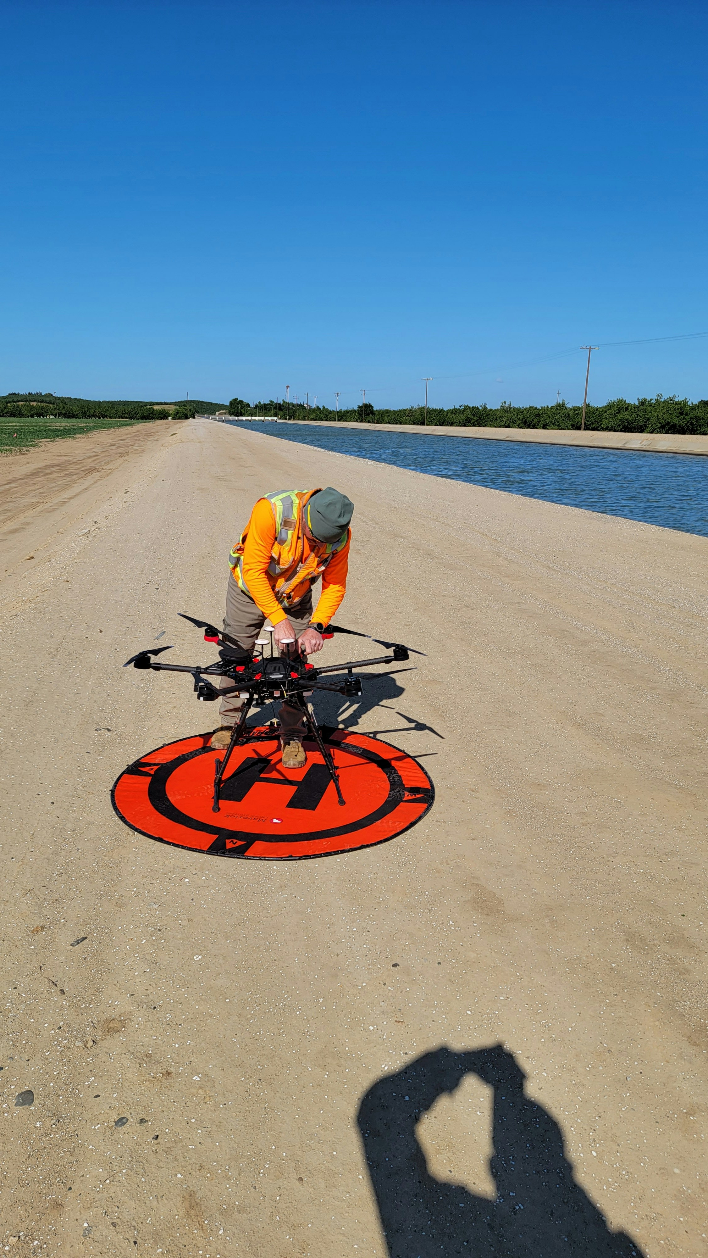 Worker setting up a multi-rotor drone on a landing pad beside a canal