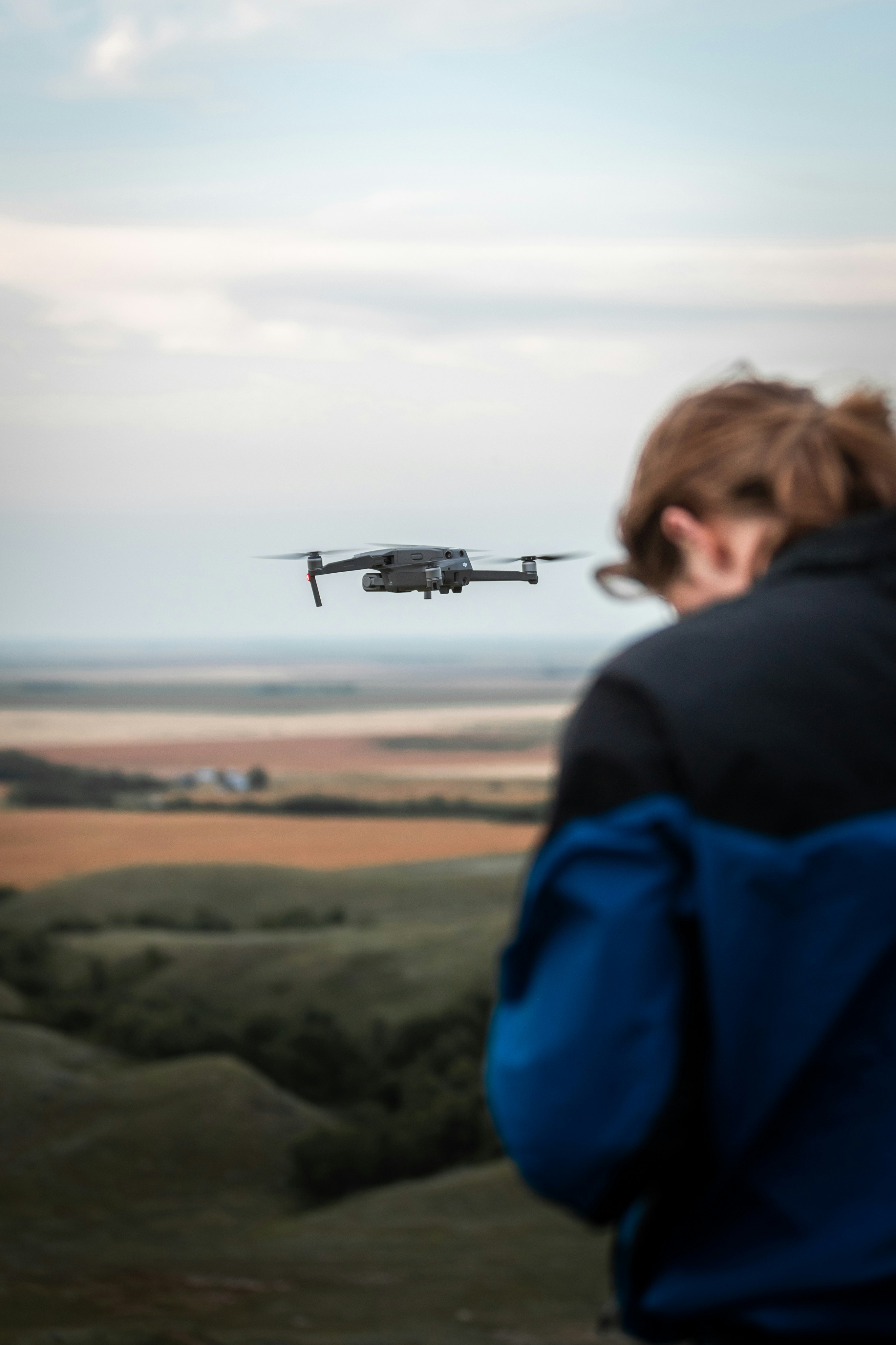 Woman looking up at a hovering drone with open farmland in the background