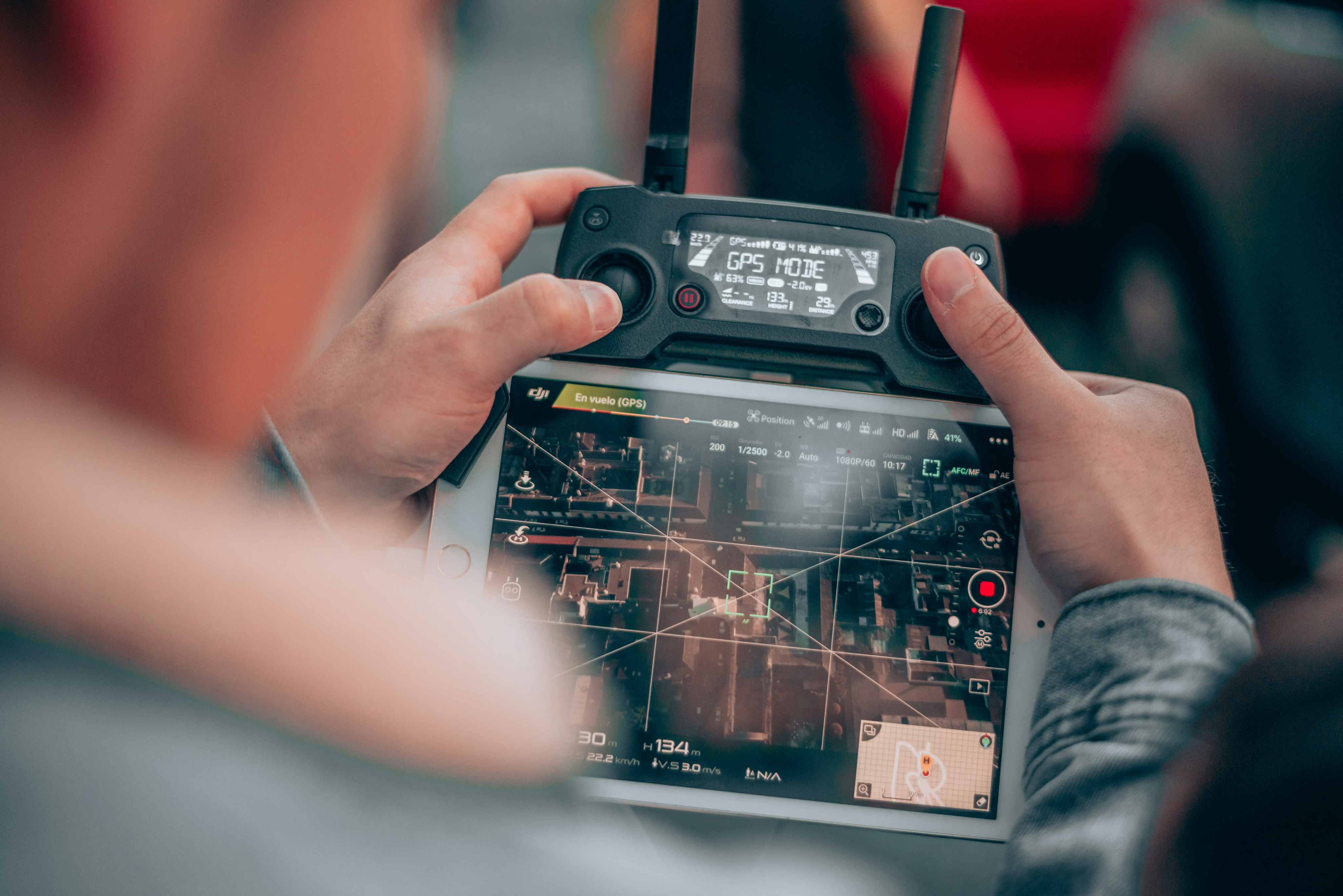 Person holding a DJI drone controller with tablet showing live aerial footage in GPS flight mode