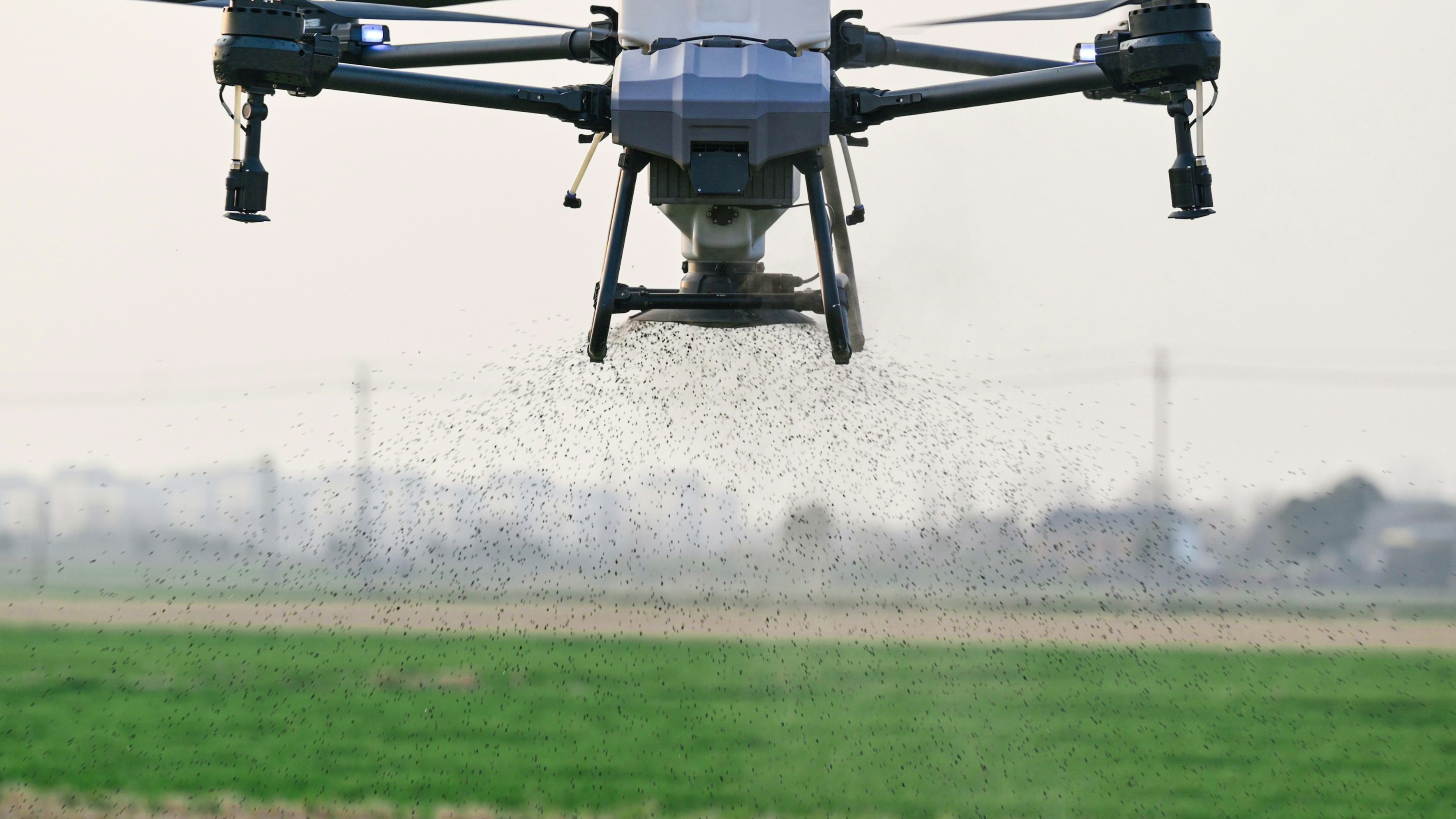Close-up of an agricultural spray drone releasing a fine mist over a green field.