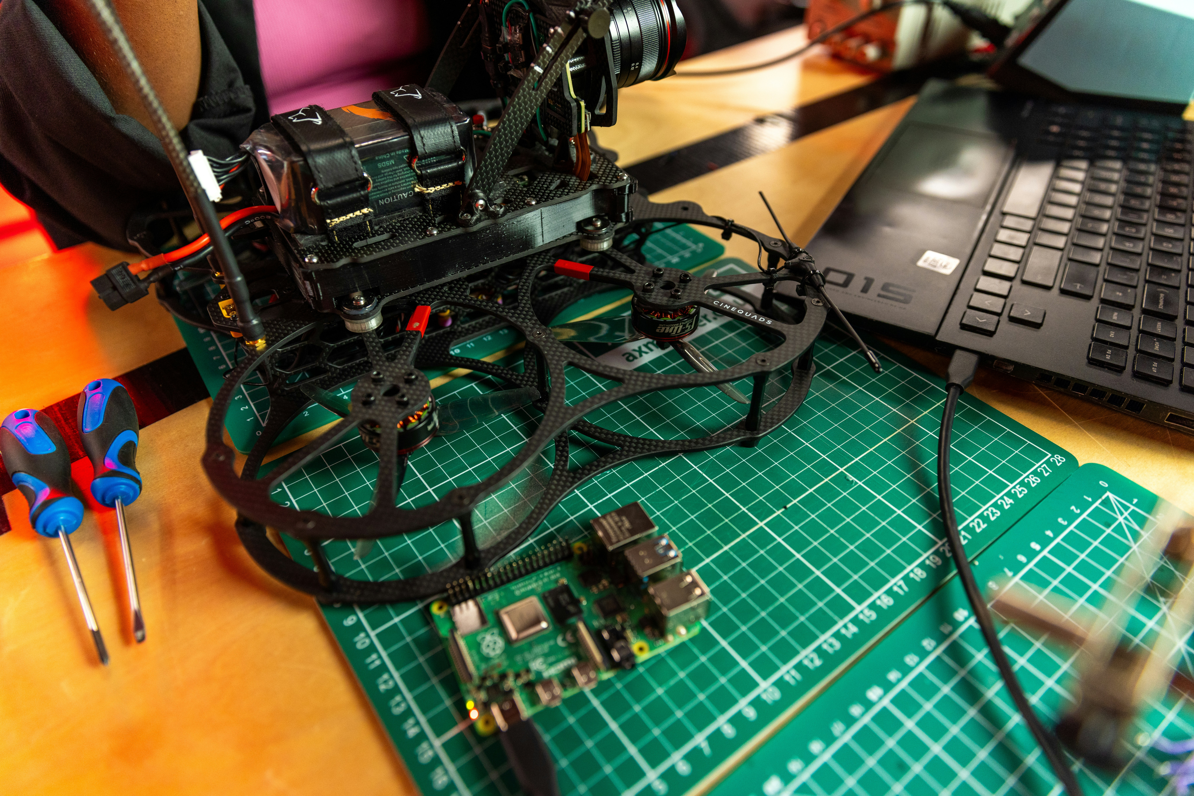 Camera drone on a repair mat with screwdrivers, a Raspberry Pi, and a laptop nearby