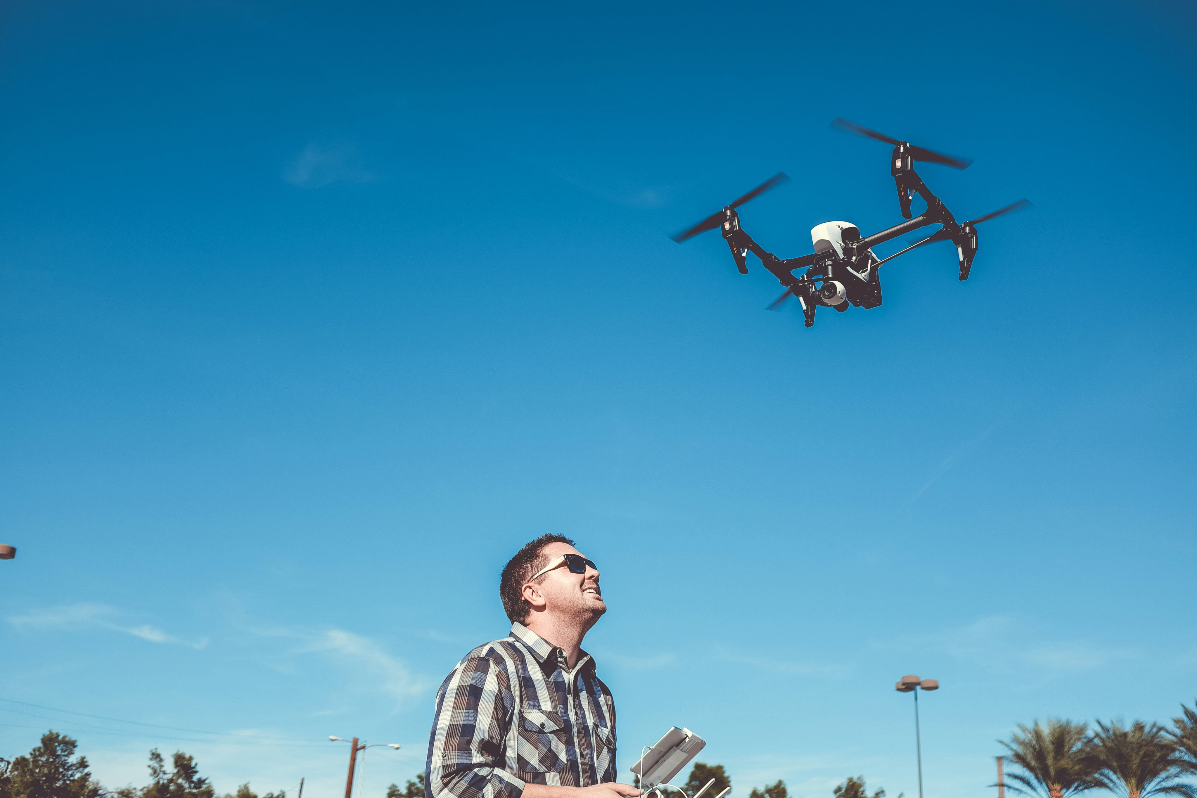 Smiling man flying a drone against a clear blue sky